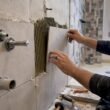 Manos colocando azulejos y accesorios en el baño