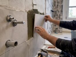 Manos colocando azulejos y accesorios en el baño