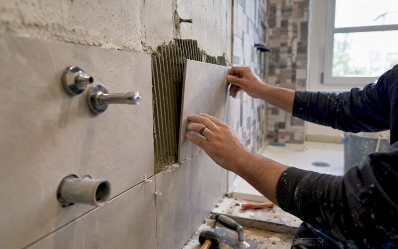 Manos colocando azulejos y accesorios en el baño
