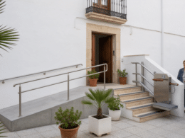 Entrada accesible de edificio residencial con rampa, plataforma salvaescaleras y barandillas